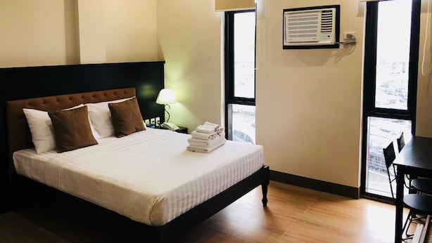 A hotel room with a bed, bedside table, lamp, air conditioning unit, and a view through the window.