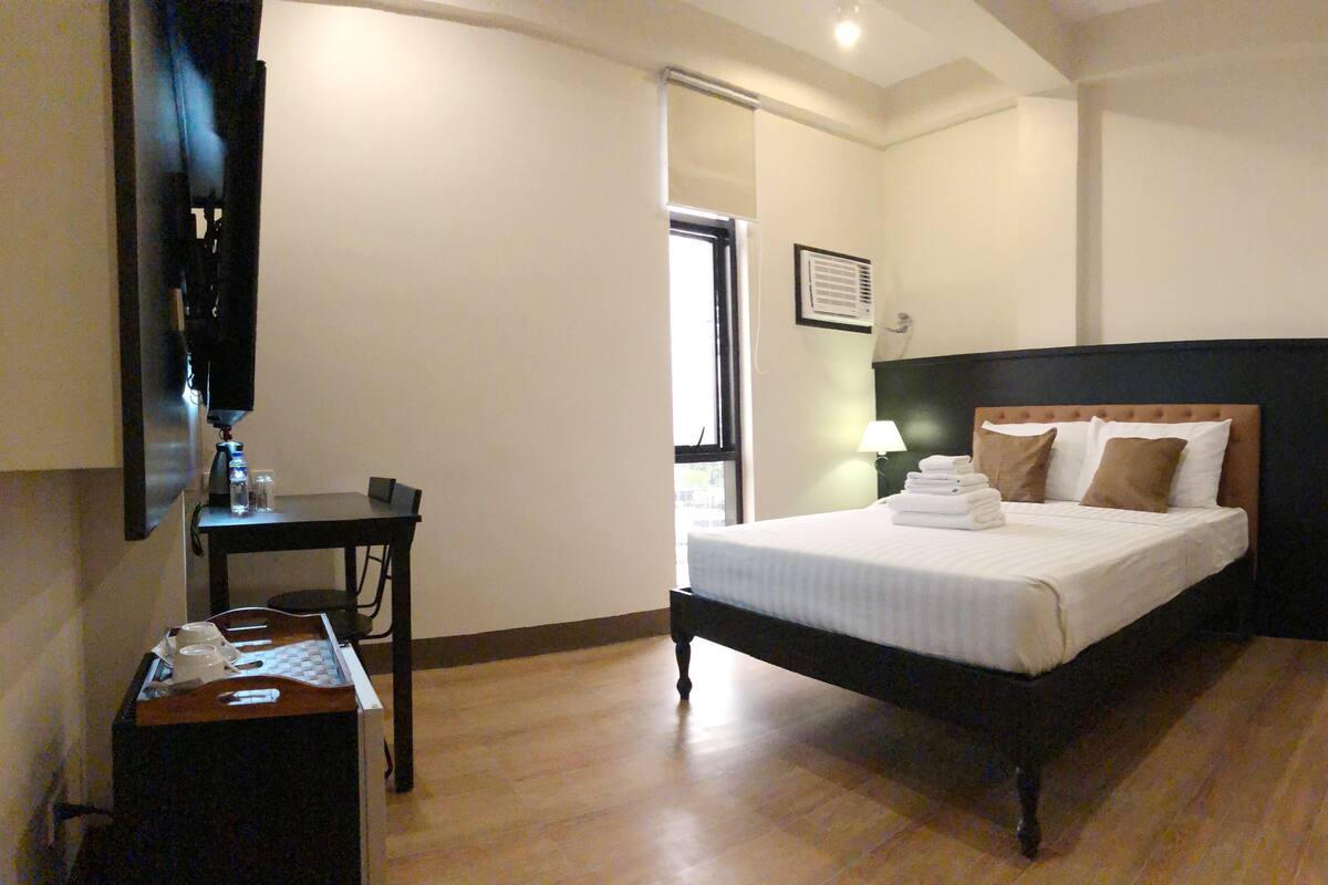 A hotel room with a bed, a desk, a chair, a mirror, and a window.