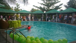 A swimming pool with a person in the water, surrounded by onlookers and green umbrellas. - La Parola Orchids Beach Resort (Patnongon)