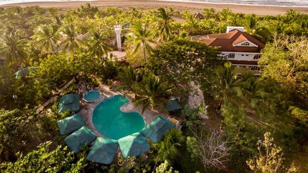 Une propriété située en bord de mer, dotée d’une piscine, de palmiers et d’une grande maison.