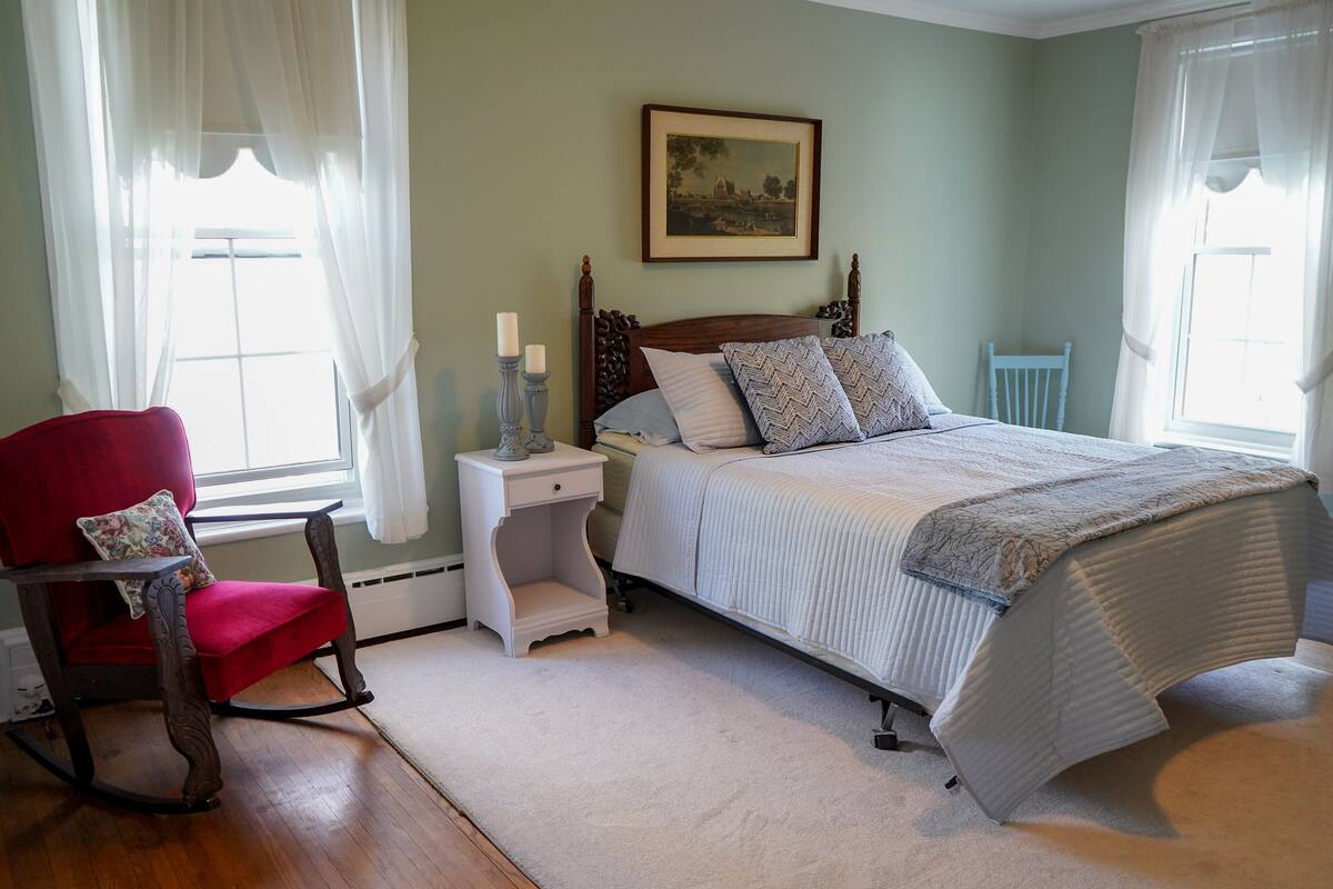 A bedroom with a bed, a rocking chair, a nightstand, and a framed picture on the wall.