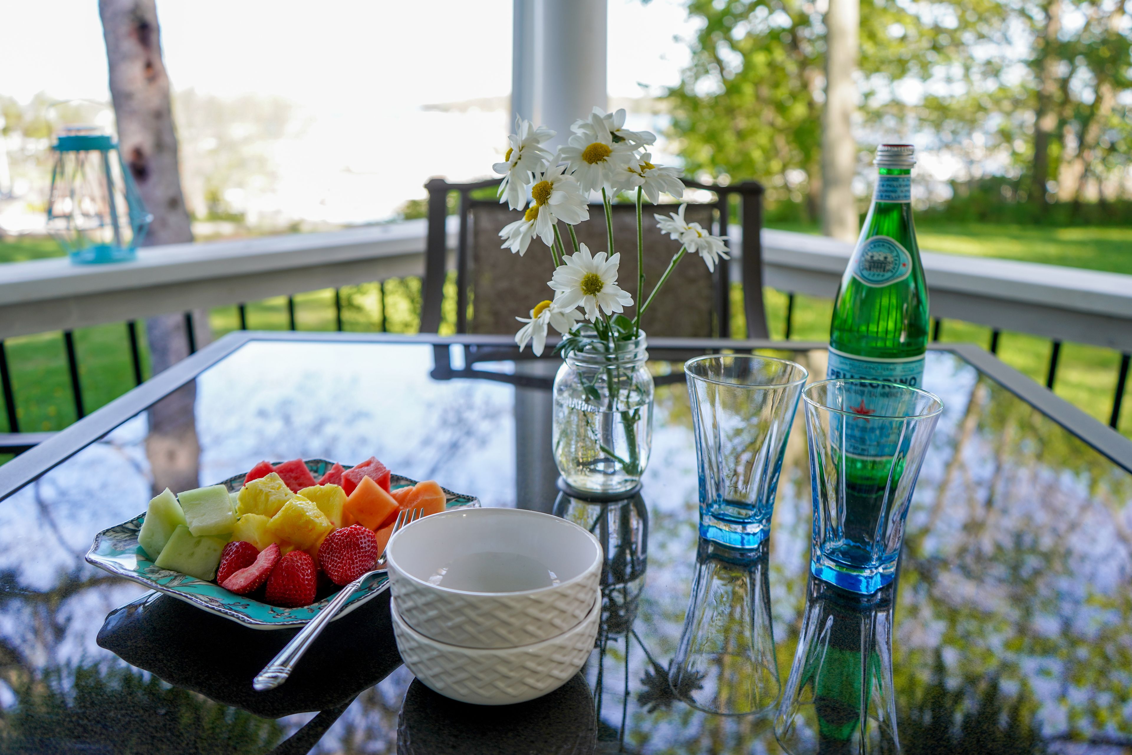 Ein Tisch mit einer Obstschale, einer Blumenvase und einer Wasserflasche.