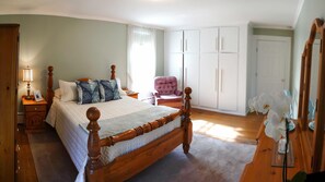 A bedroom with a wooden four-poster bed, a nightstand with a lamp, a chair, a wardrobe, and a mirror. - Waterside Inn (Gananoque)