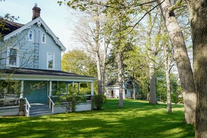 A light blue house with a porch, surrounded by a well-maintained lawn and tall trees. - Waterside Inn (Gananoque)