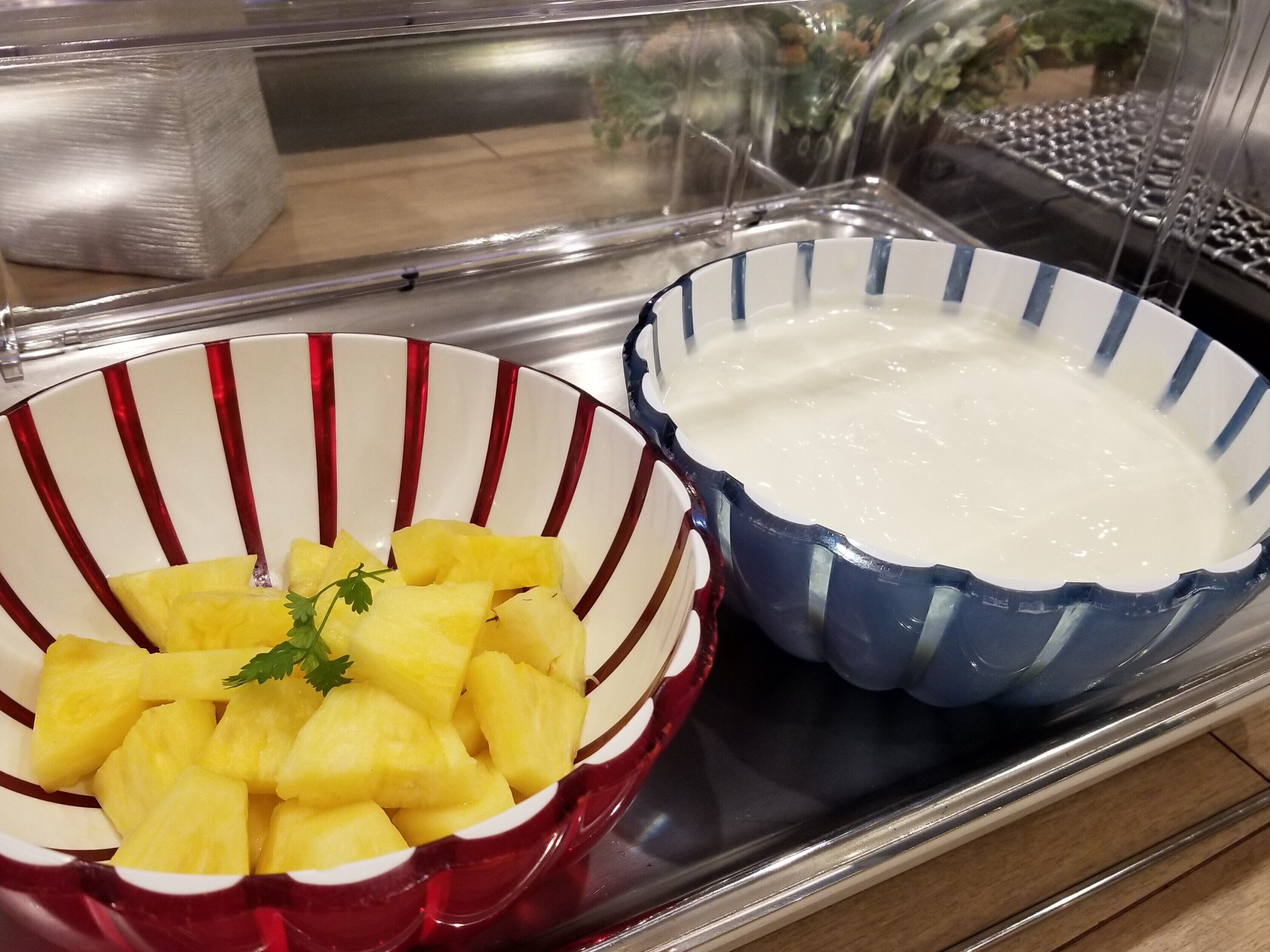 A buffet tray with two bowls, one containing pineapple chunks and the other a creamy white substance, possibly a dip or dressing.