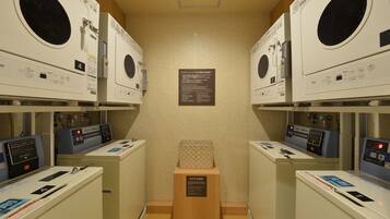 A laundry facility with multiple washing machines, a central informational sign, and a wooden stool.