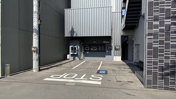 A parking area with a 'STOP' sign painted on the ground, a metal structure to the left, and a building entrance with a staircase to the right.