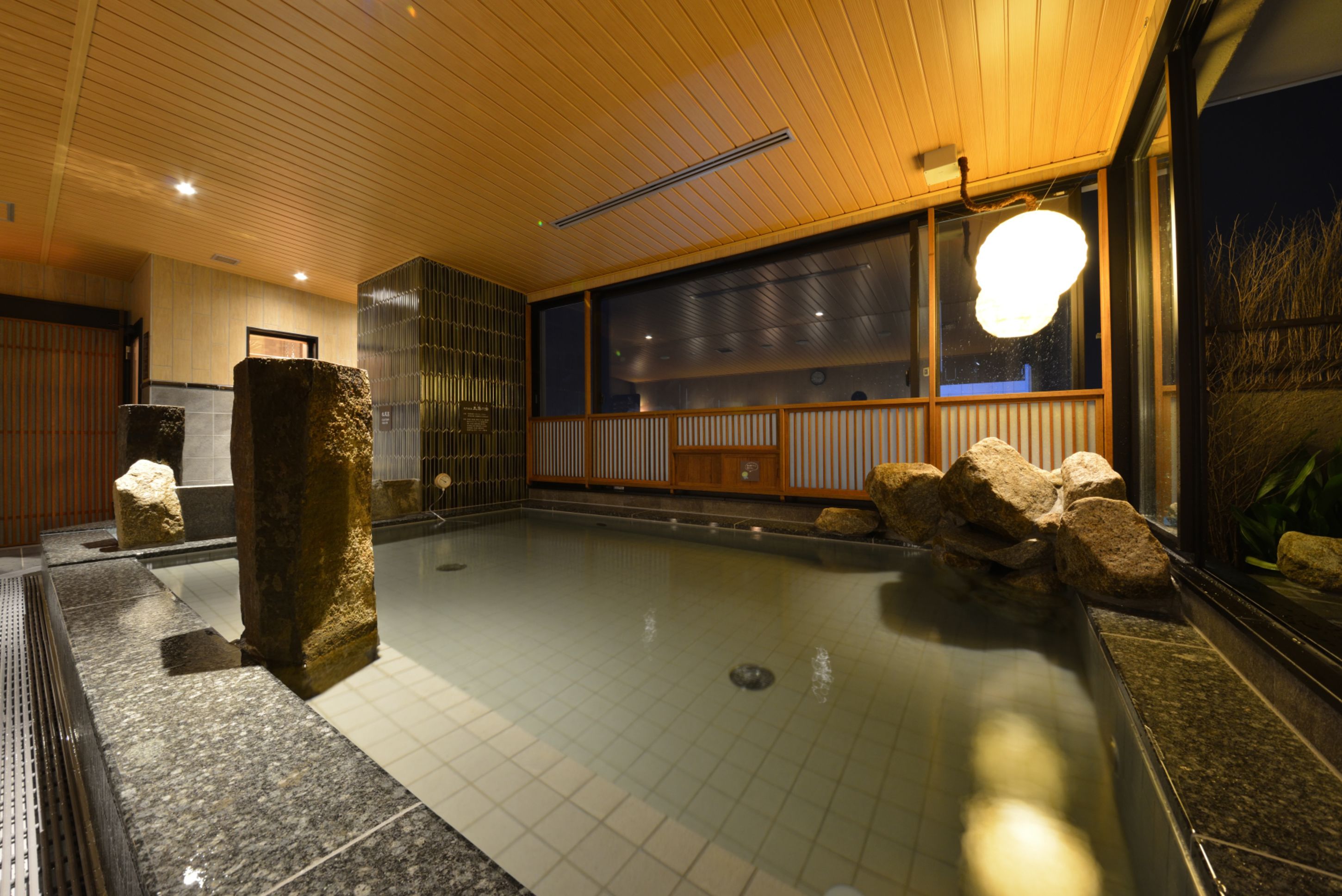 A traditional Japanese onsen with a wooden ceiling, tiled floor, and a large window.