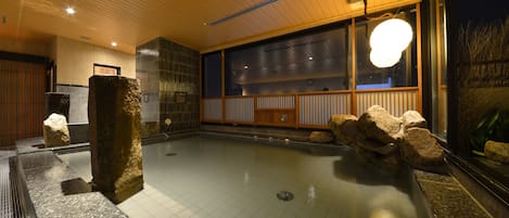 Un onsen japonés tradicional con techo de madera, suelo de baldosas y un ventanal grande.
