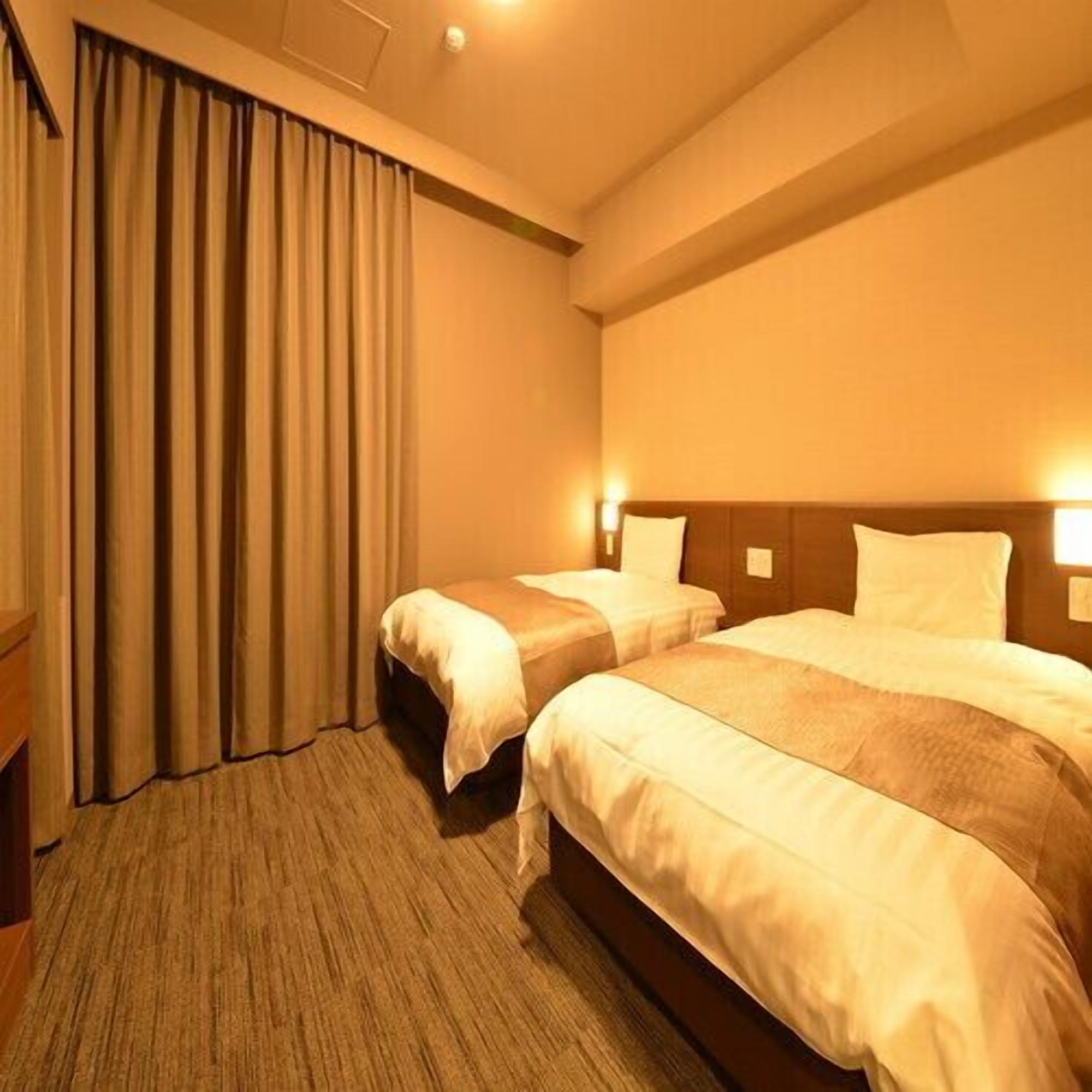 A hotel room with two beds, a large window with curtains, and a carpeted floor.