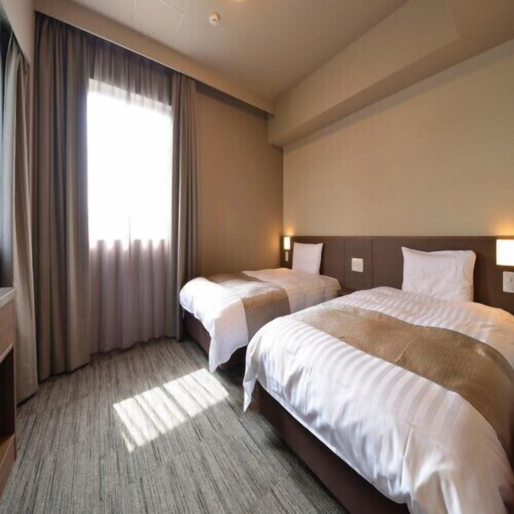 Ein Hotelzimmer mit zwei Betten, einem großen Fenster mit Vorhängen und einem Teppichboden.