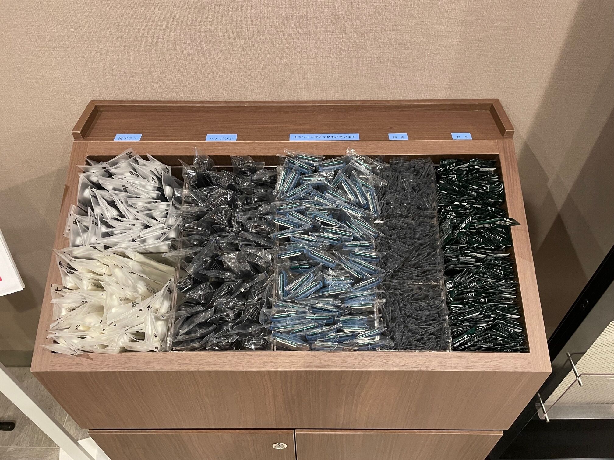 A wooden drawer with multiple compartments containing various items, each labeled with a blue tag.