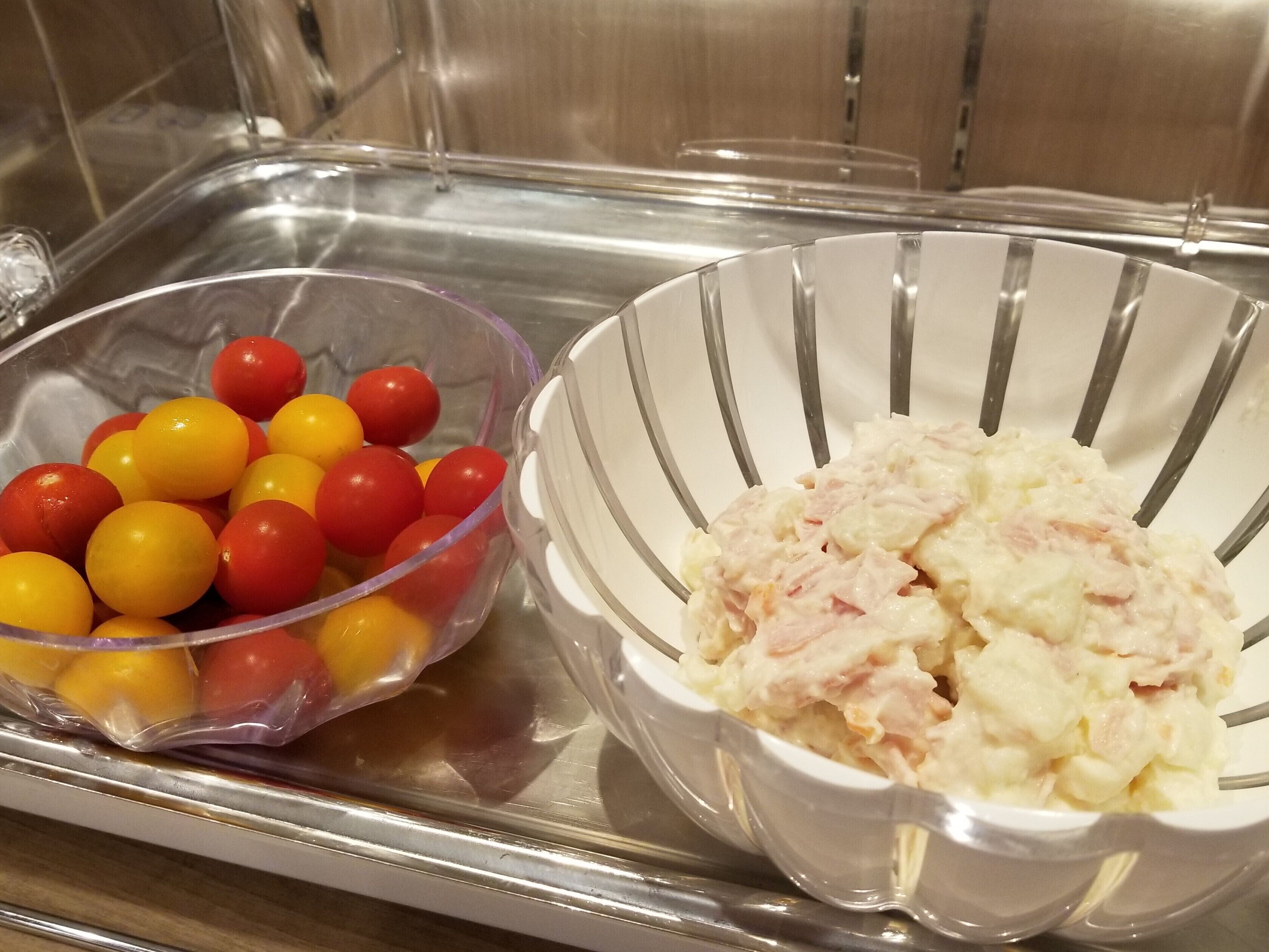 A stainless steel tray with two bowls, one containing cherry tomatoes and the other a creamy salad.