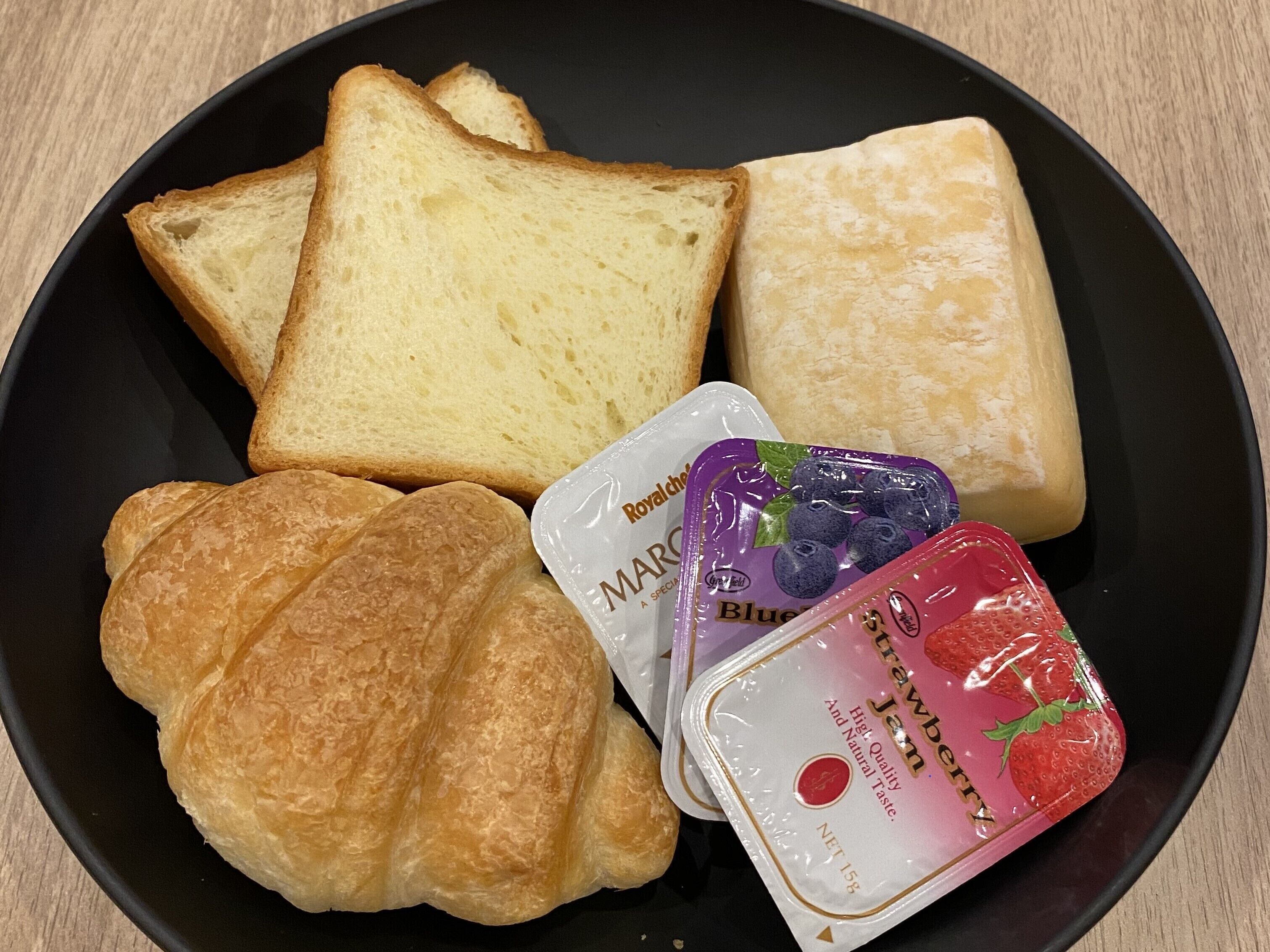 A plate with slices of bread, a croissant, and two packets of jam.