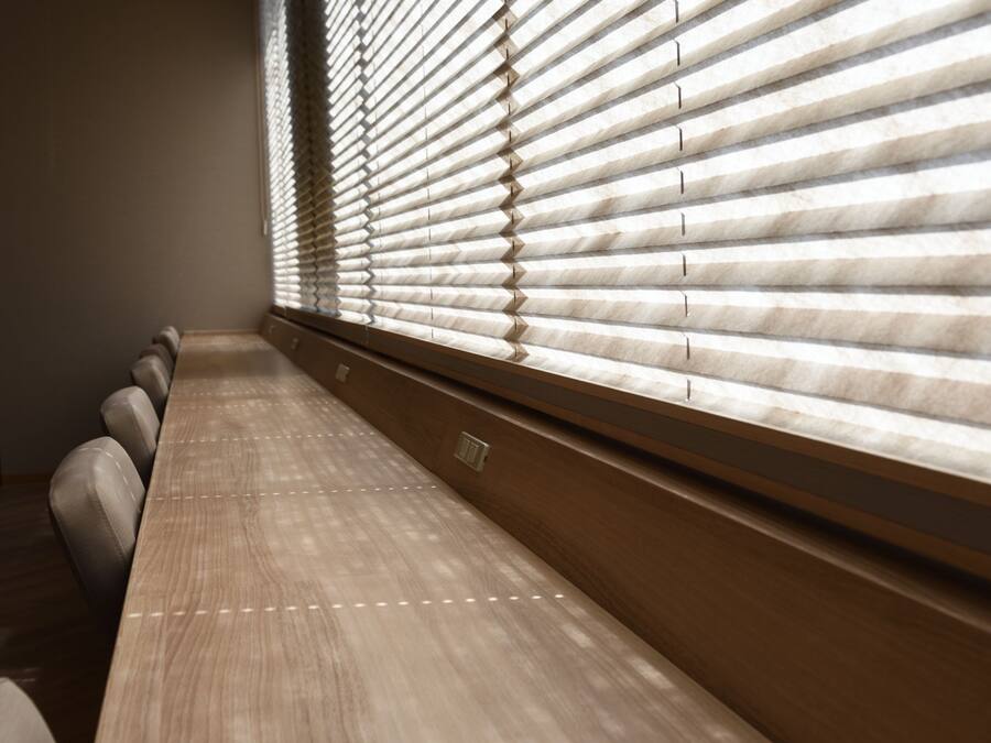 Un salón de conferencias con una larga mesa y sillas, ventanas amplias con persianas y piso de madera.