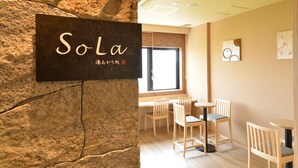 A room with a stone wall, a sign reading "Sola", wooden chairs, and a window.