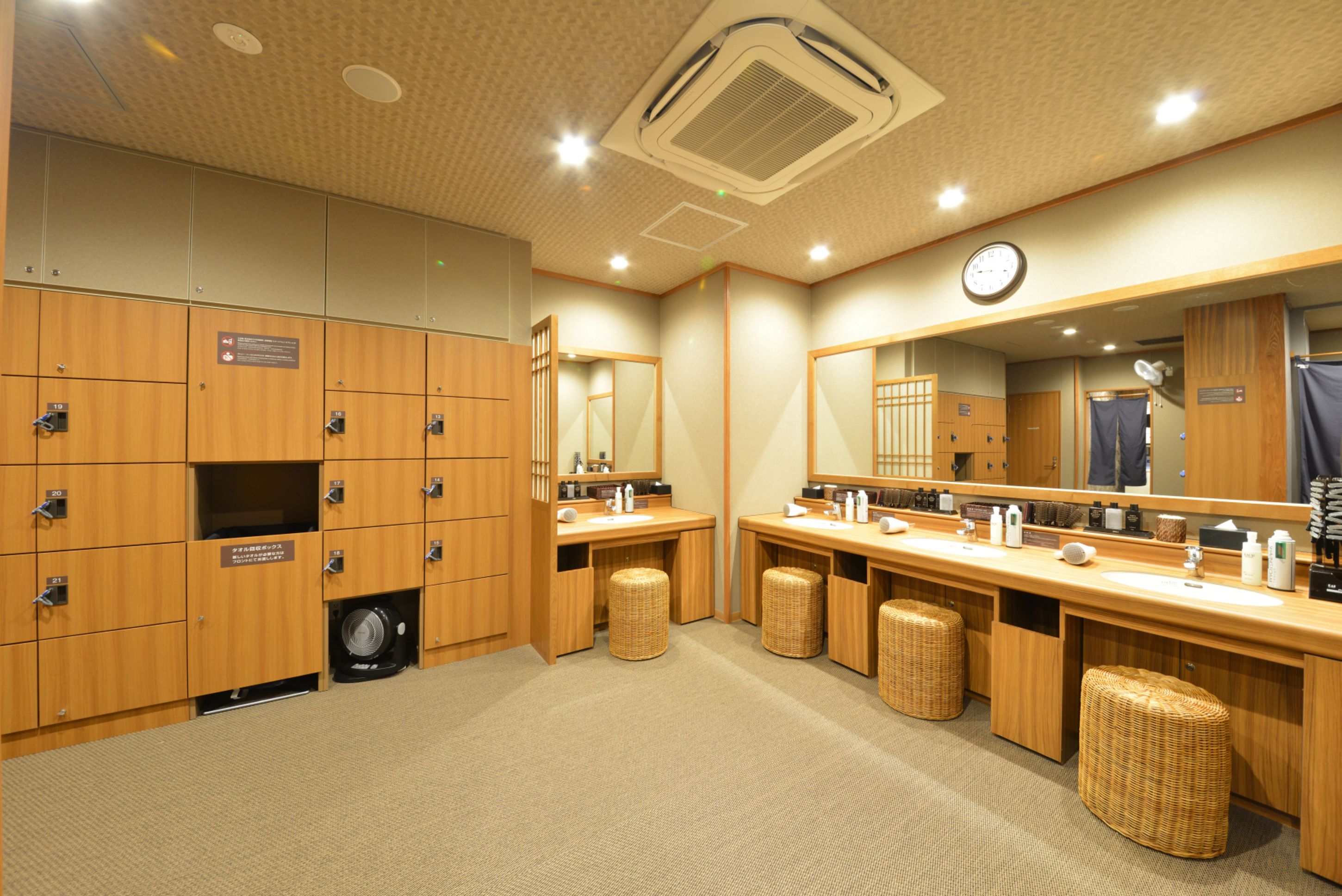 A hotel bathroom with wooden lockers, a sink, a mirror, and a clock.