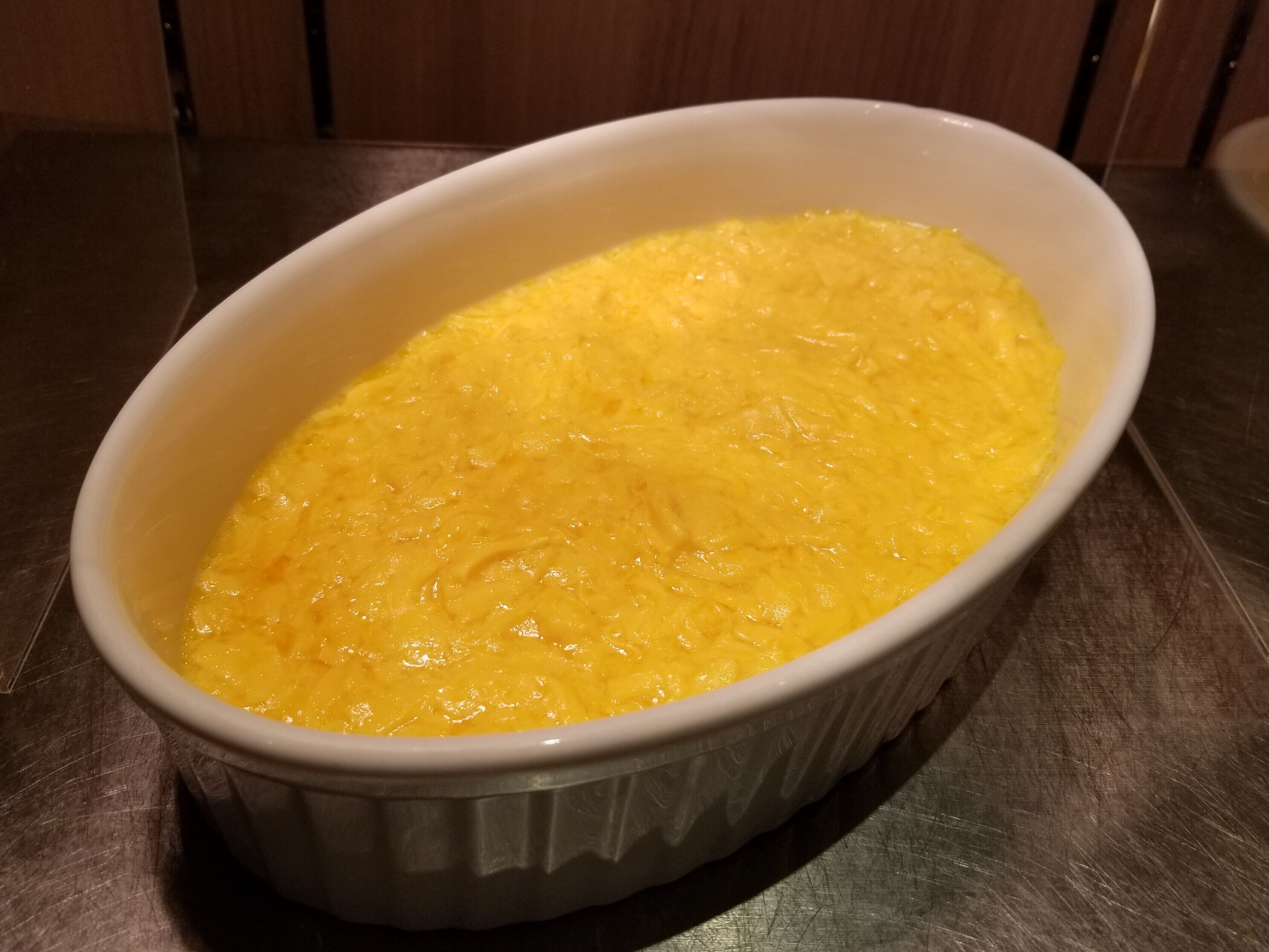 A white oval dish containing a yellow food item, possibly a casserole, on a metallic surface.