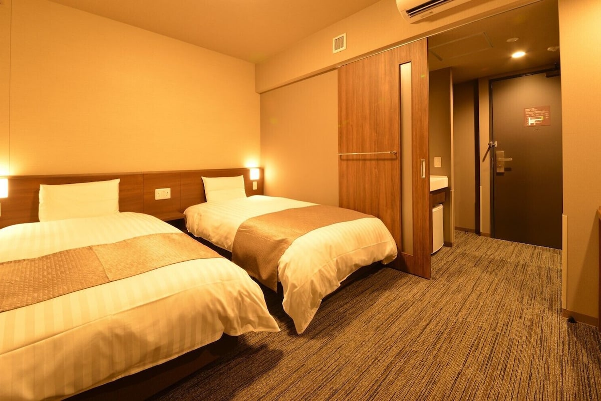 Une chambre d’hôtel avec deux lits, une armoire en bois, un bureau et un appareil de climatisation.