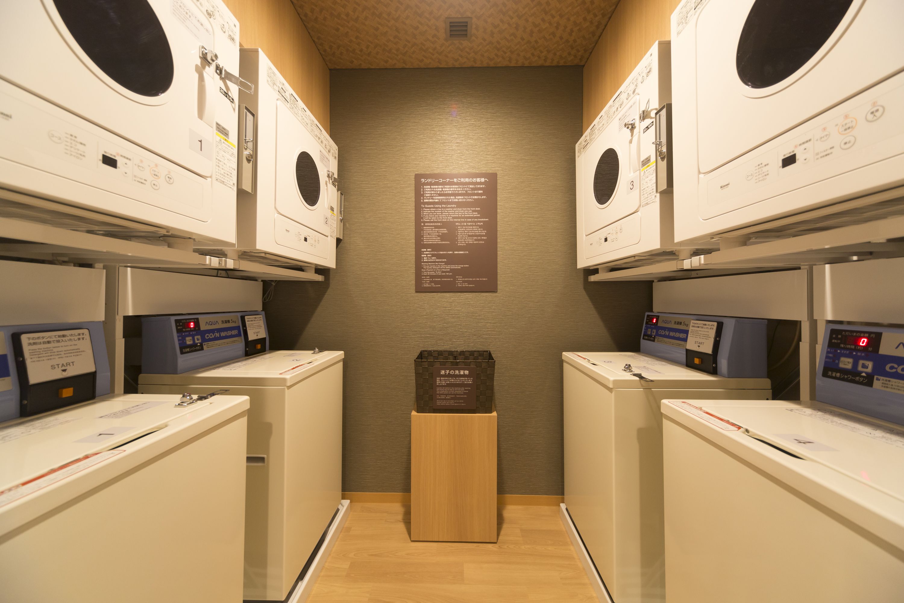 A laundry facility with multiple washing machines and dryers, a wooden floor, and a wall-mounted instruction sign.