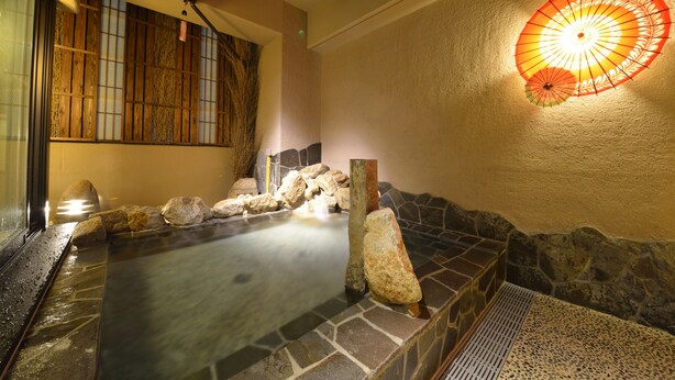 A hot spring area with a stone bath, rocks, and a wooden wall with a window.