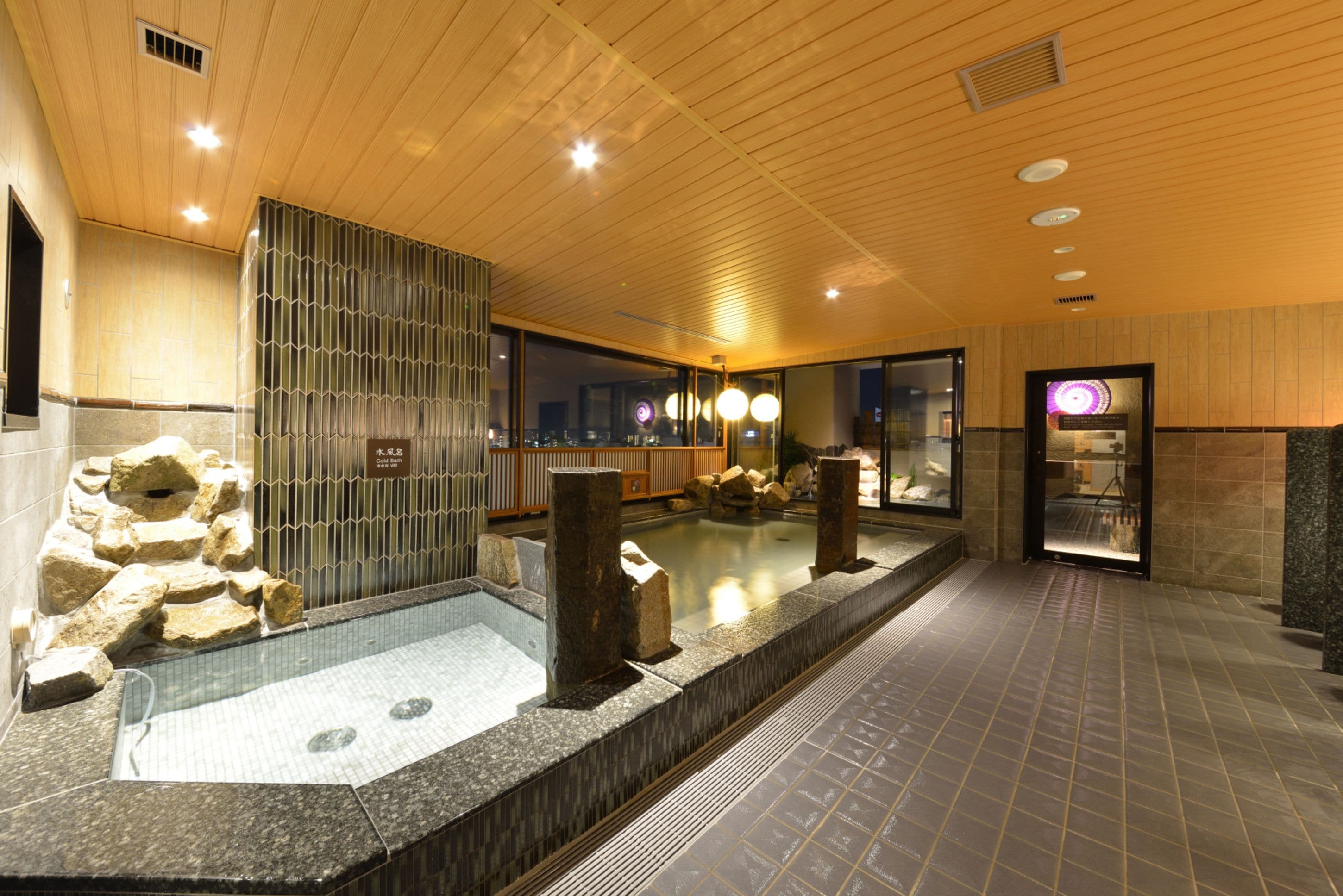 Un área de piscina interior moderna con techo de madera, paredes de piedra y una división de vidrio.