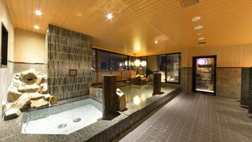 Un área de piscina interior moderna con techo de madera, paredes de piedra y una división de vidrio.