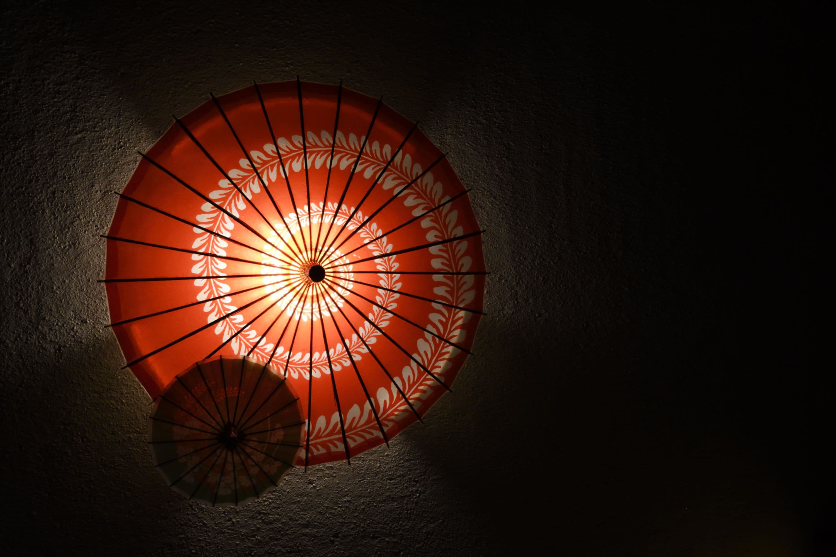 Een aan de muur bevestigd, rood-wit decoratief paraplu met een lichtbron in het midden.