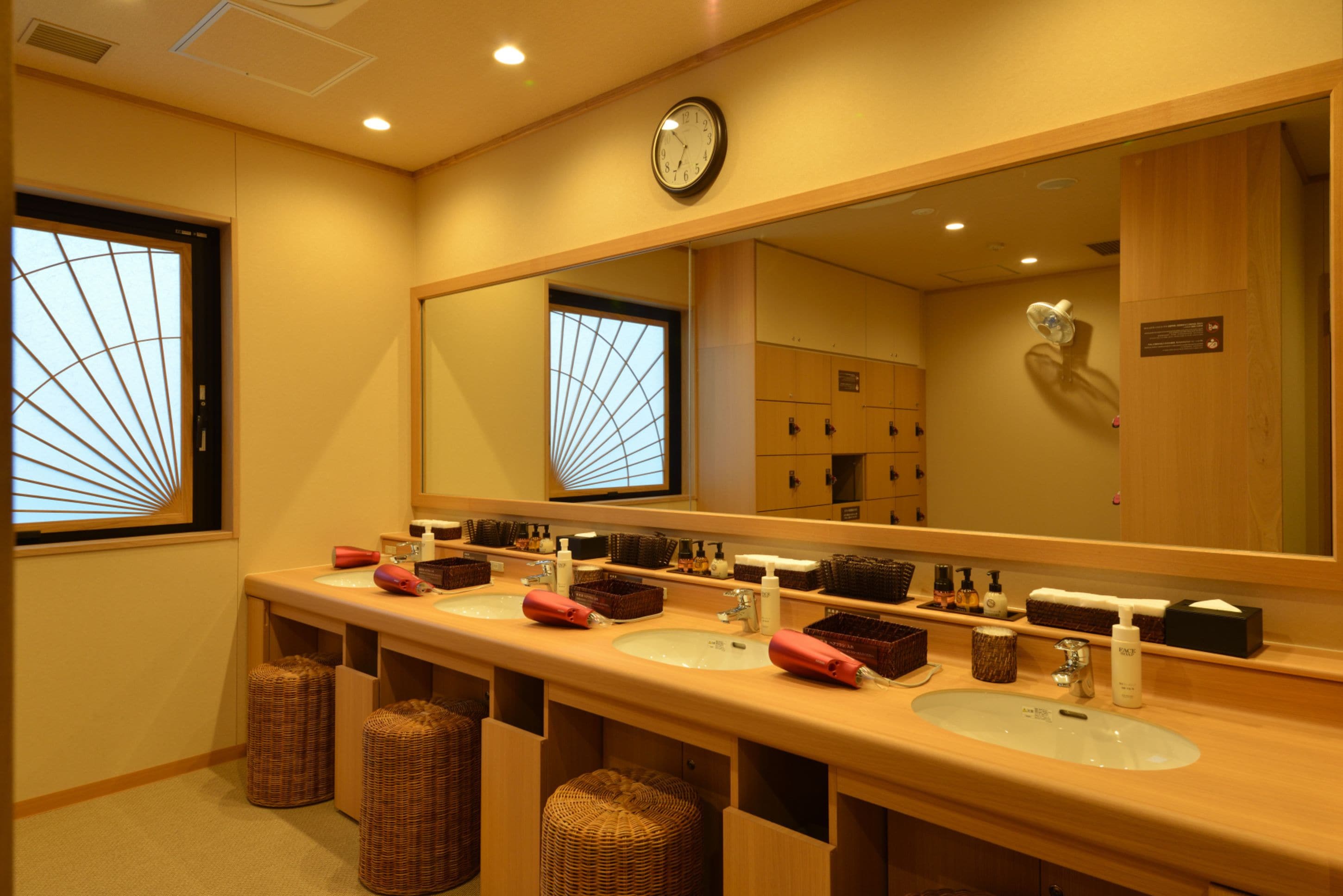 Une salle de bain d’hôtel avec deux lavabos, un grand miroir et une horloge au mur.