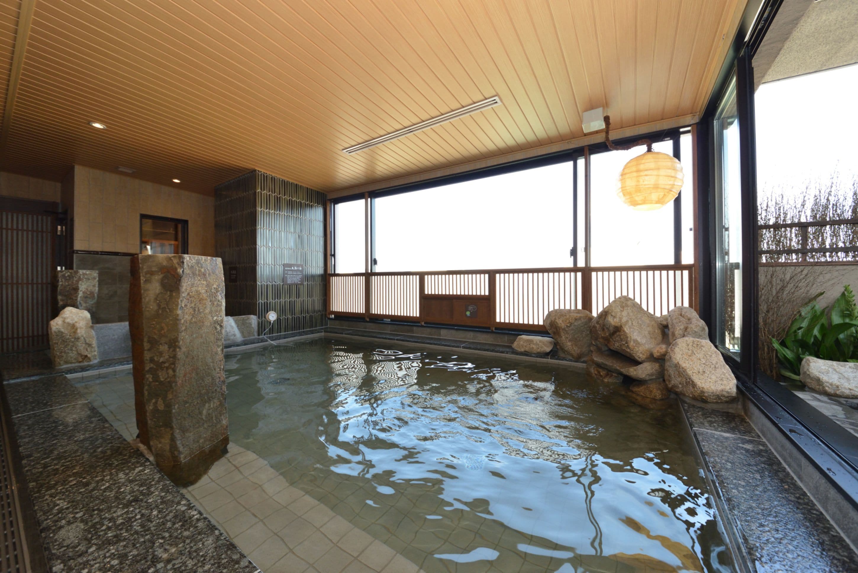A traditional Japanese onsen with a wooden ceiling, a stone basin, and a view of the outdoors.