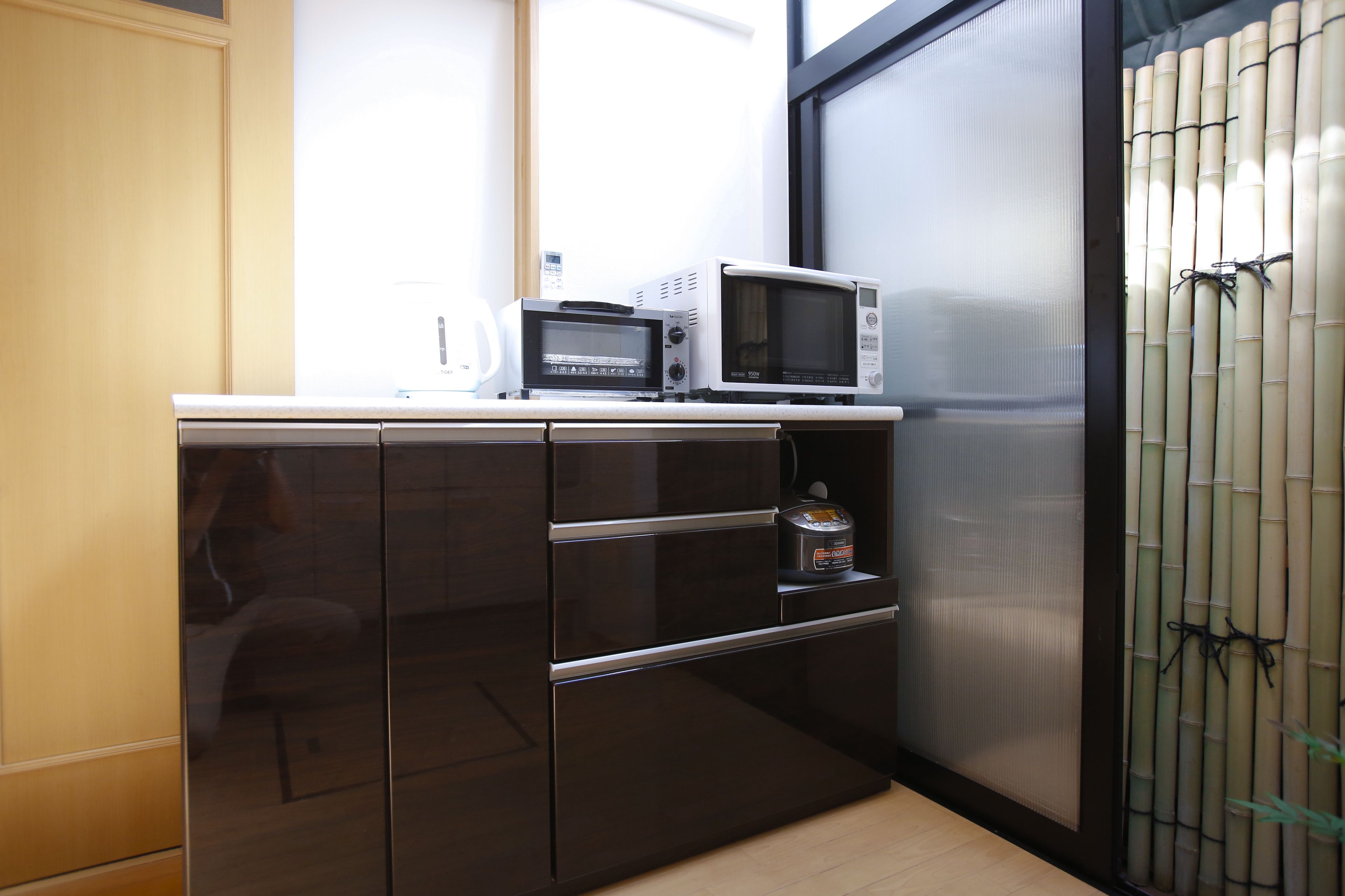 A compact kitchen with a microwave, a small refrigerator, and a bamboo screen.