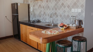 A compact kitchen with a wooden countertop, a sink, a stove, and a refrigerator. There are two stools and a decorative bowl on the counter. - KAEN Apartments (Cemagi)