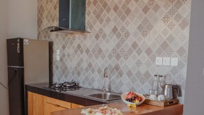 A kitchen with a wooden countertop, a sink, a stove, and a refrigerator. There are two green bar stools and a green pendant light above the counter. - KAEN Apartments (Cemagi)