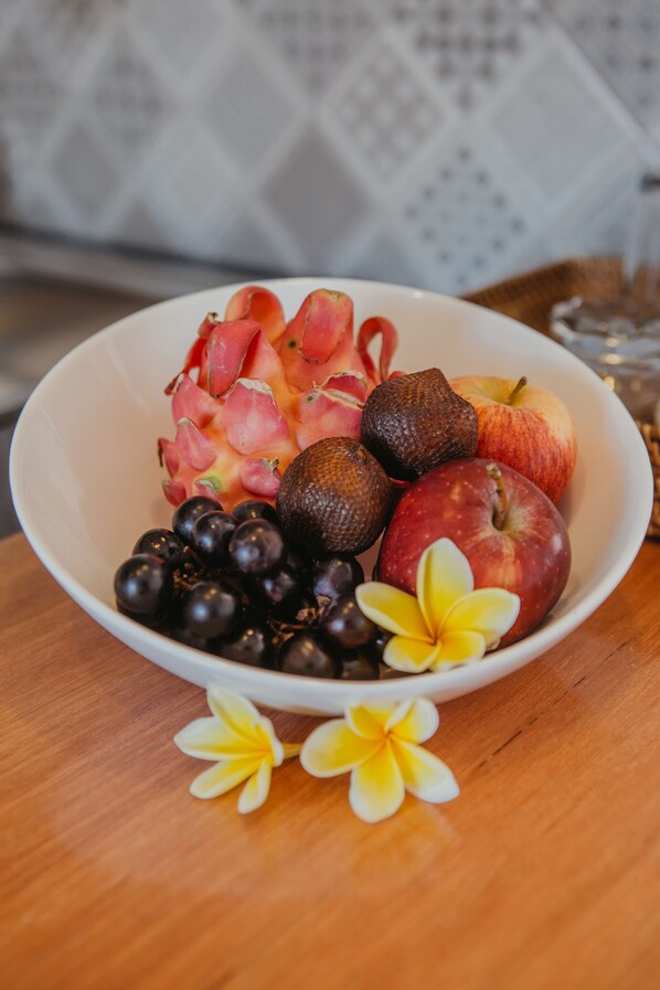 Un tazón con frutas variadas y flores de plumeria sobre una mesa de madera.