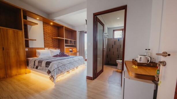 A modern bedroom with a large bed, wooden shelving, and a small kitchenette. - KAEN Apartments (Cemagi)