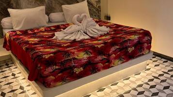 Una cama con colcha floral, dos almohadas y una toalla sobre la misma. La habitación tiene un suelo con estampado geométrico y un cabecero de mármol.