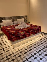 Una cama con colcha floral, dos almohadas y una toalla sobre la misma. La habitación tiene un suelo con estampado geométrico y un cabecero de mármol.