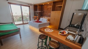 A modern hotel room with a bed, a small sofa, a dining table with stools, a kitchen area, and a balcony with a view. - KAEN Apartments (Cemagi)