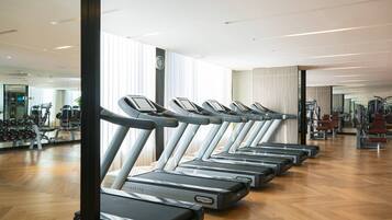 Eine Reihe von Laufbändern in einem Fitnessstudio mit Holzboden und großen Fenstern.
