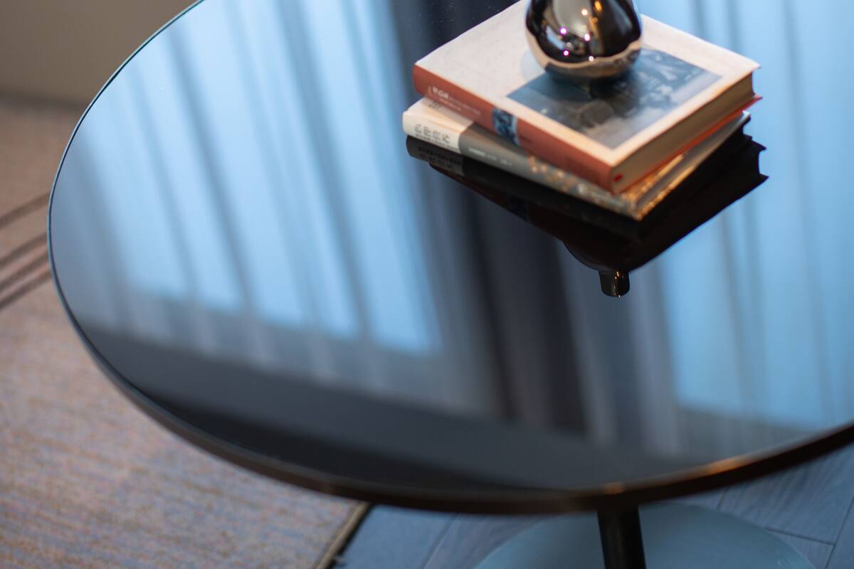 A modern living room with a glass coffee table, a book, and a decorative vase.