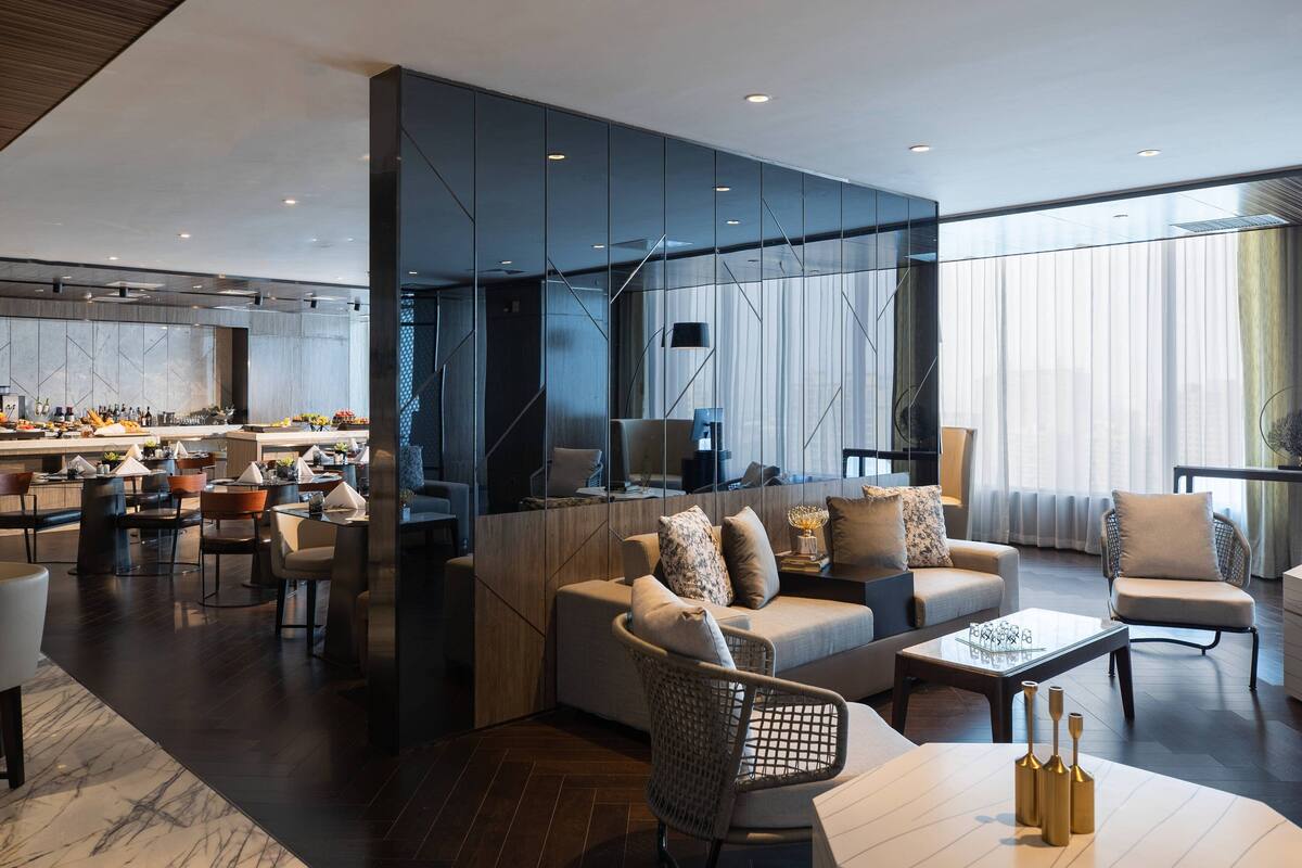 Un moderno vestíbulo de hotel con zona de comedor, asientos y un amplio ventanal que proporciona luz natural.