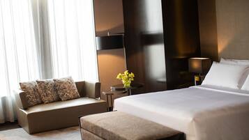 A modern hotel room with a large bed, a sofa, a small table with a vase of flowers, and a lamp.
