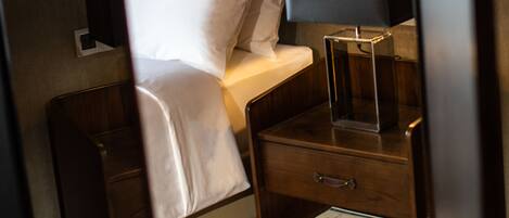 A hotel room with a bed, bedside table, lamp, and a small shelf with books.