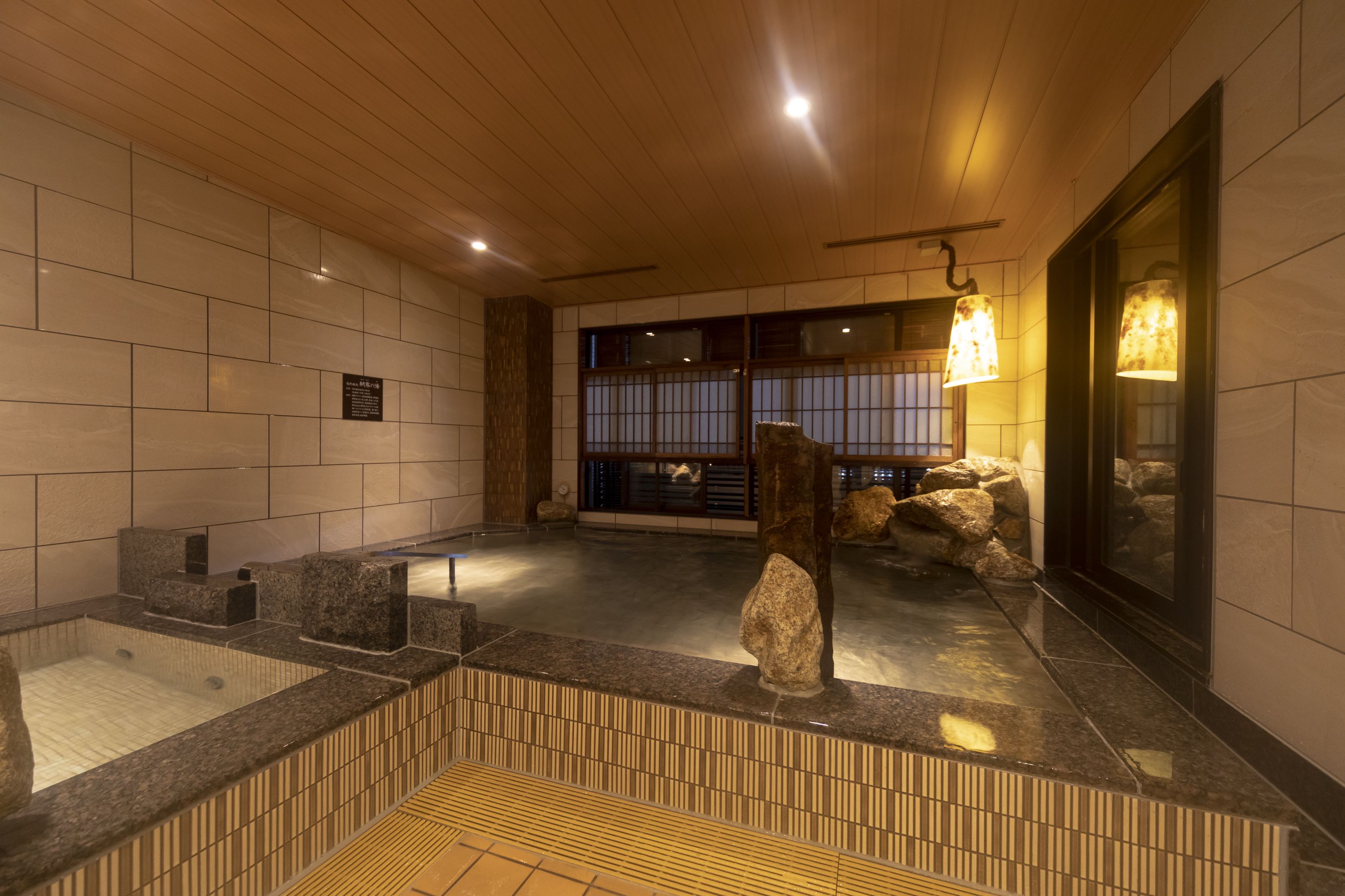 Una habitación tradicional japonesa con suelo de tatami, bañera de piedra y techo de madera.