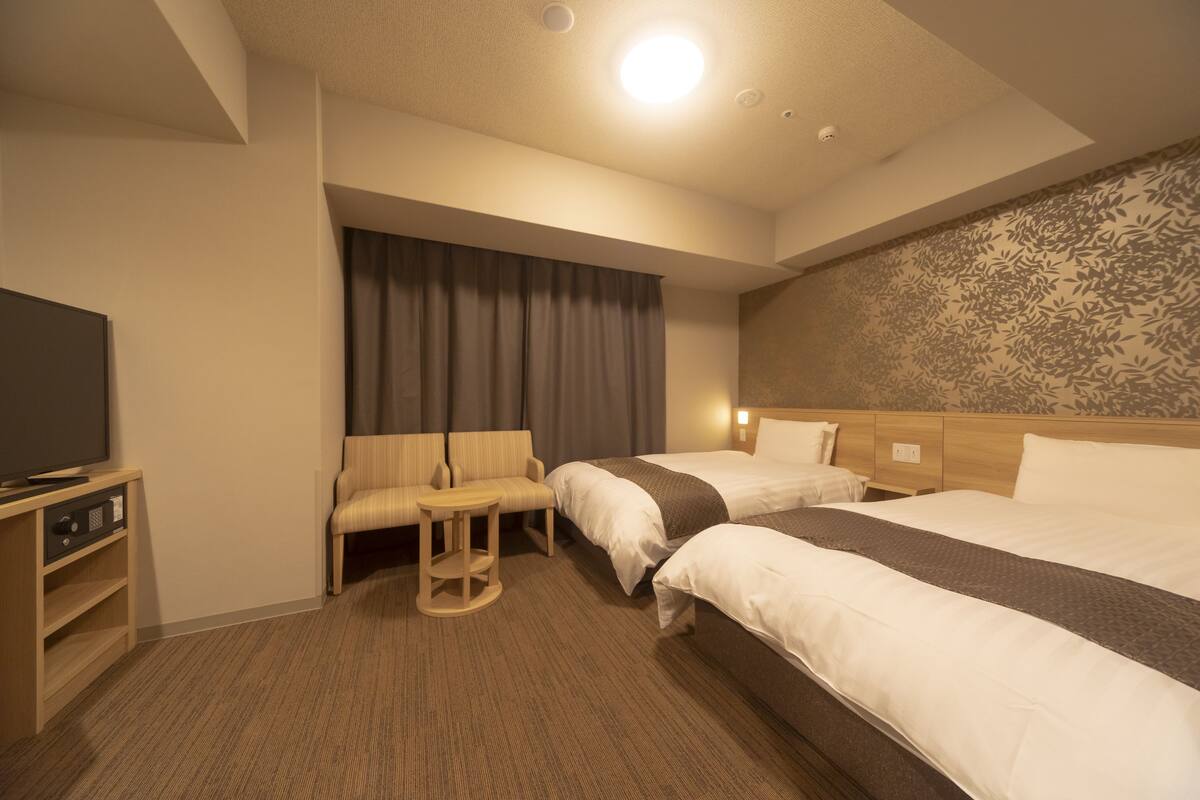 A hotel room with two beds, a TV, a sofa, and a small table.