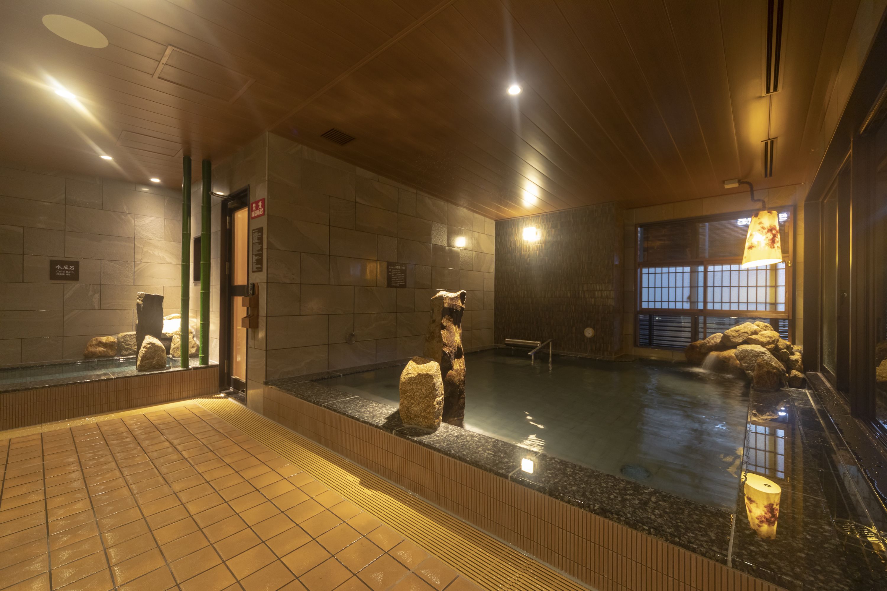 An indoor swimming pool with a wooden ceiling, tiled walls, and a glass barrier.