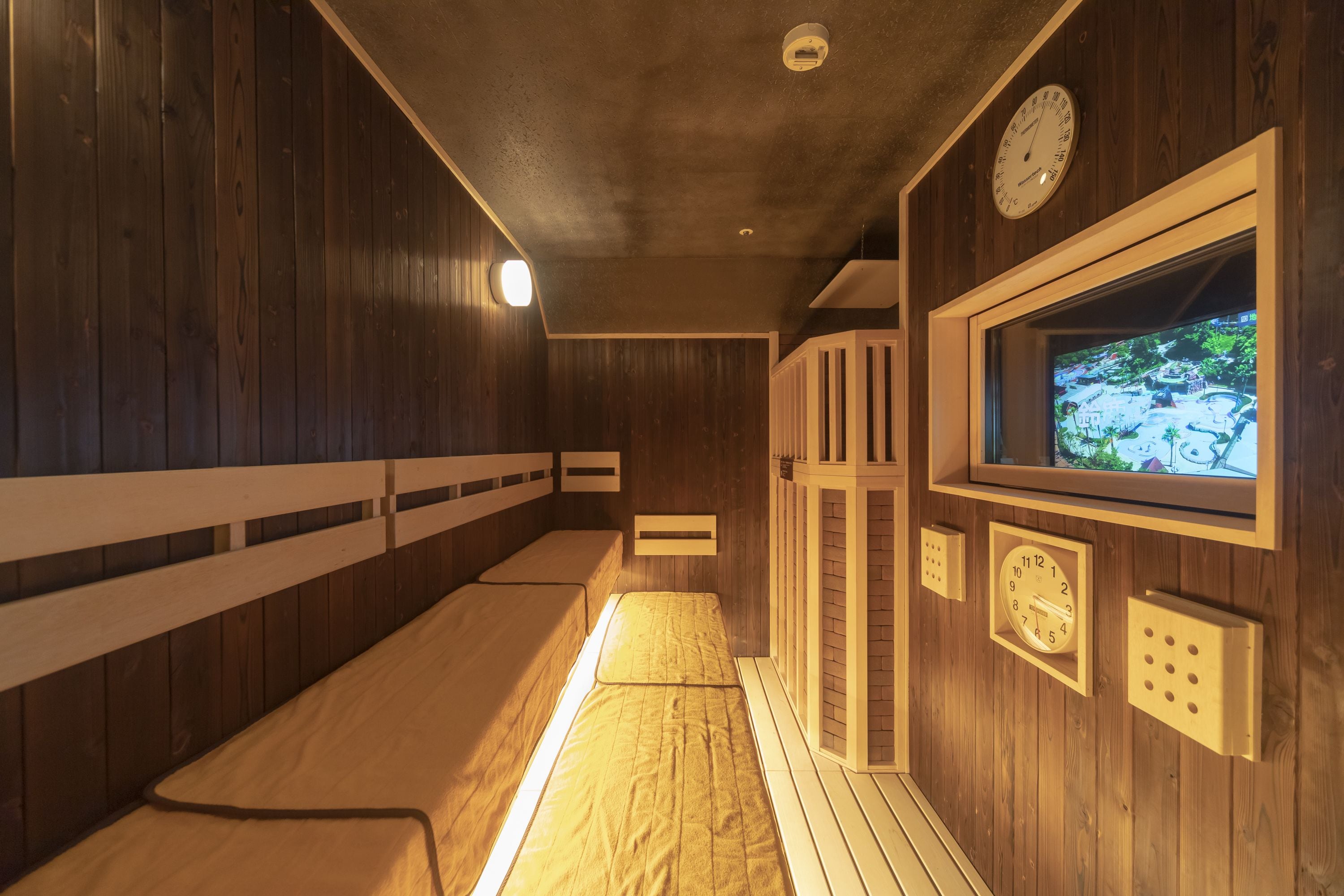 Uma sala de sauna com paredes de madeira, bancos, um relógio e uma tela de televisão.