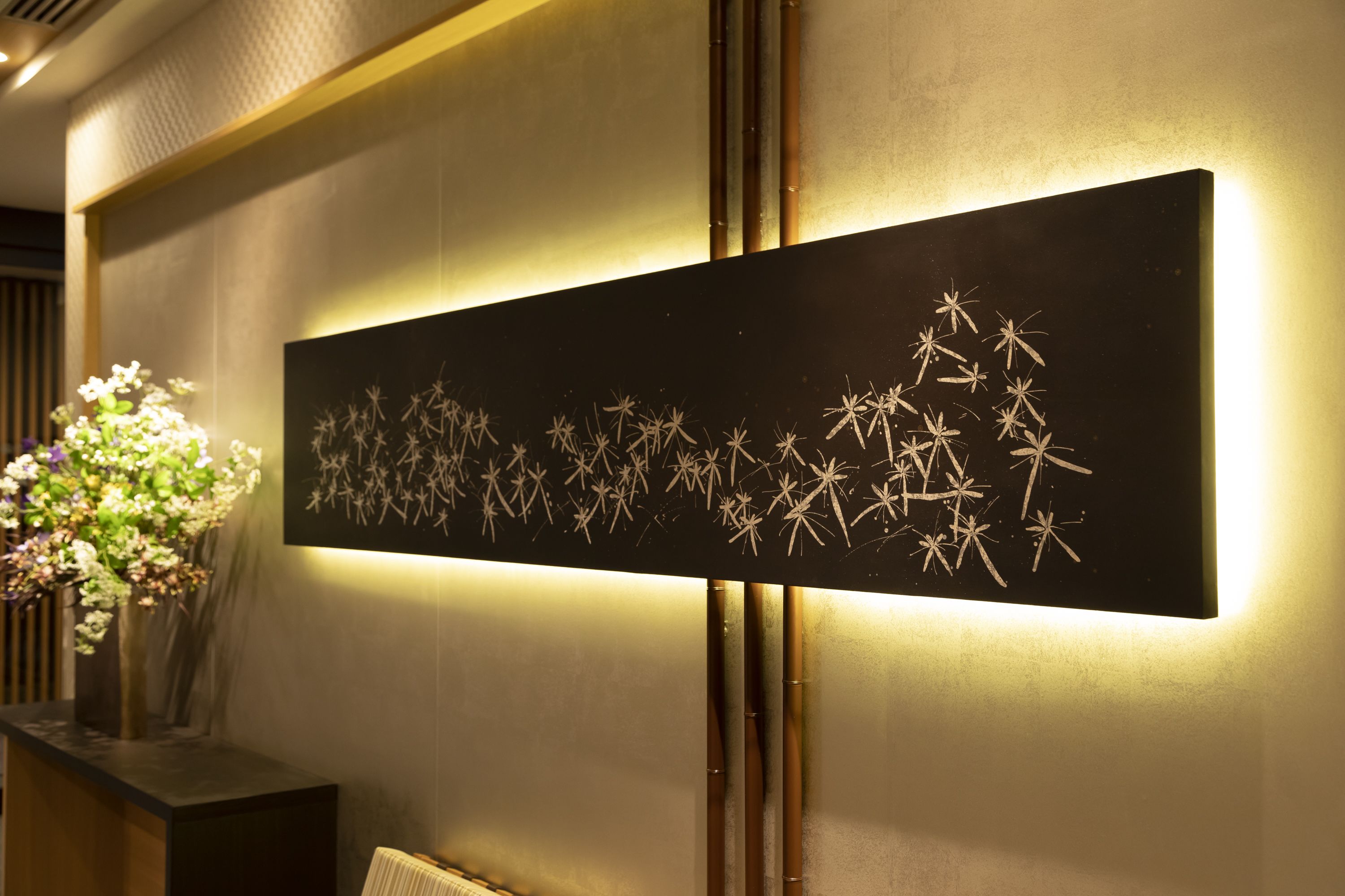 Una obra de arte colgada en la pared con diseño de bambú, un florero con flores y una consola de madera oscura.