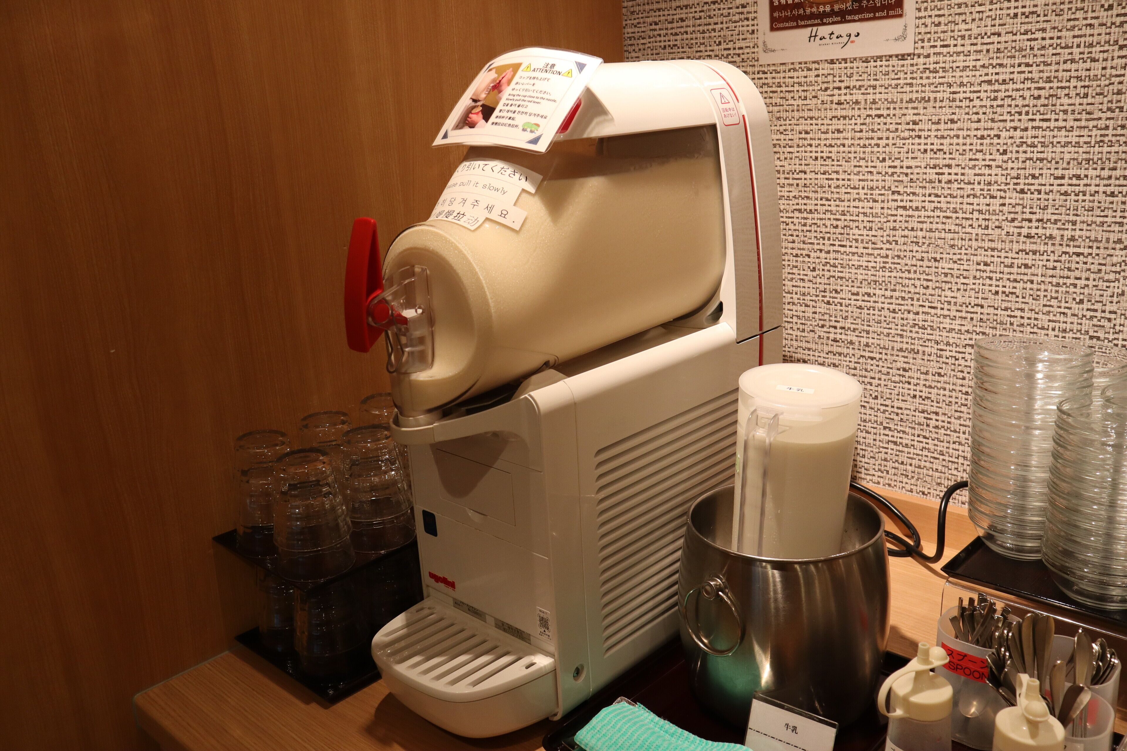 A coffee machine with a milk frother, a stainless steel pot, and a tray of disposable cups.