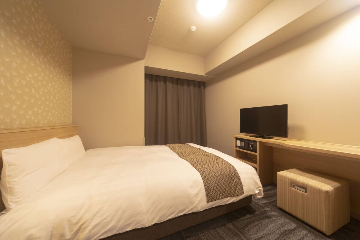 A hotel room with a bed, a television, a desk, and a storage unit.